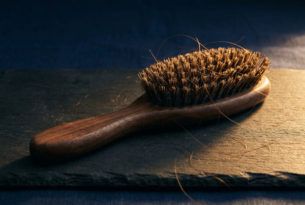 Wooden hair brush with loose strands on dark surface representing natural pumpkin seed oil hair thinning support